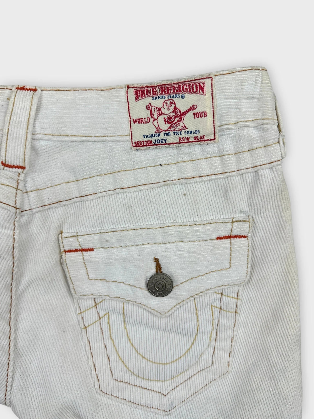 Detail view of white denim shorts featuring red stitching and logo patch.
