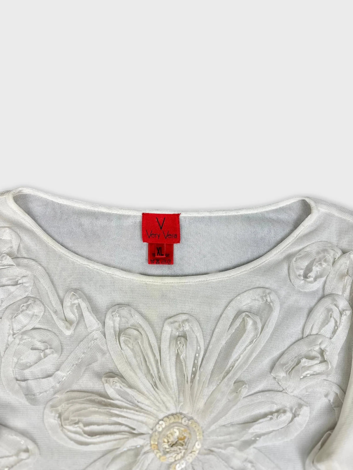 Detail view of white long sleeve top with floral embellishments.