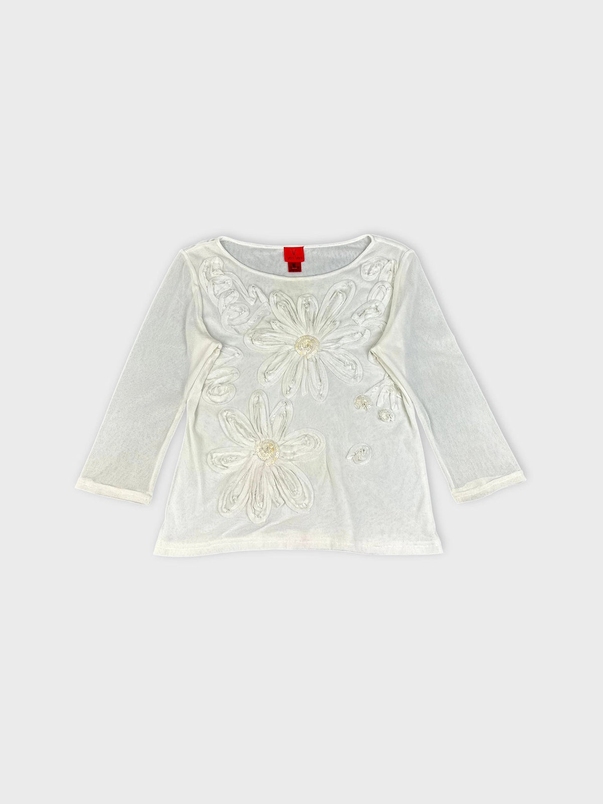 Detail view of white long sleeve top with floral embellishments.