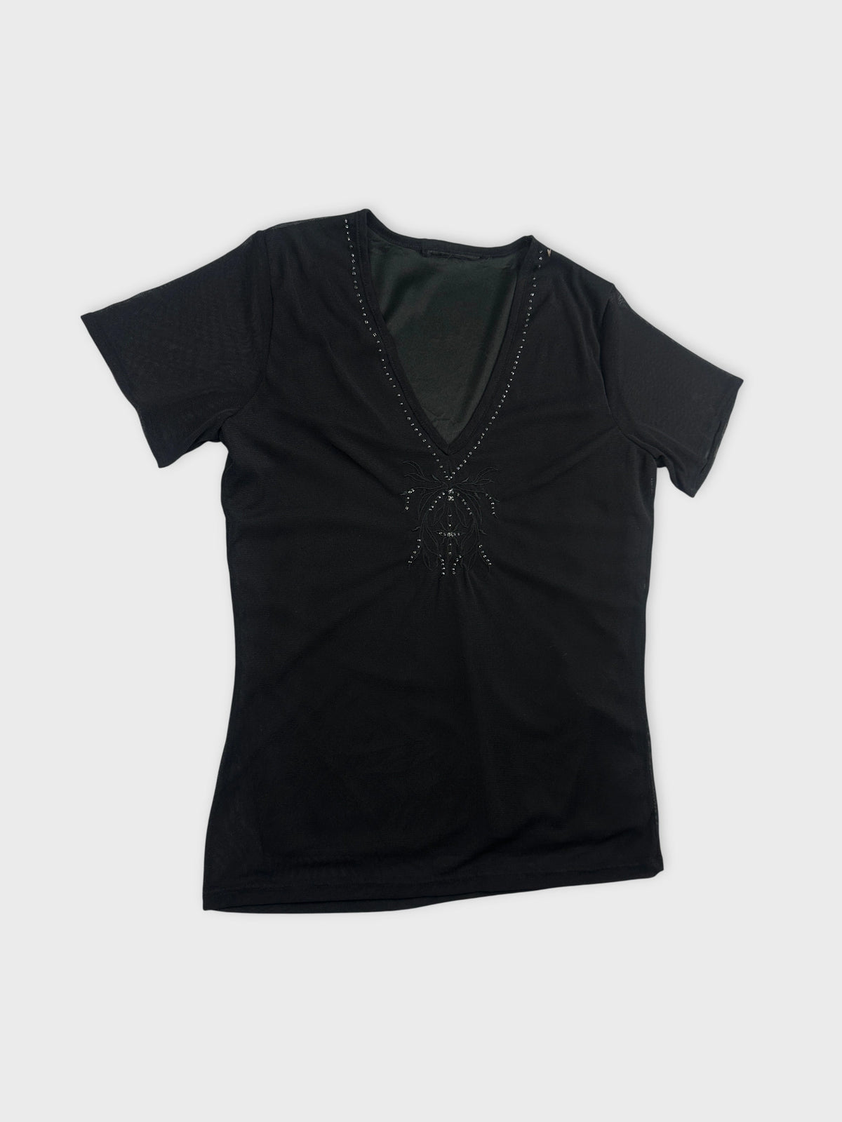 Detail view of a black women’s body shirt with a V-neck and embellishment.