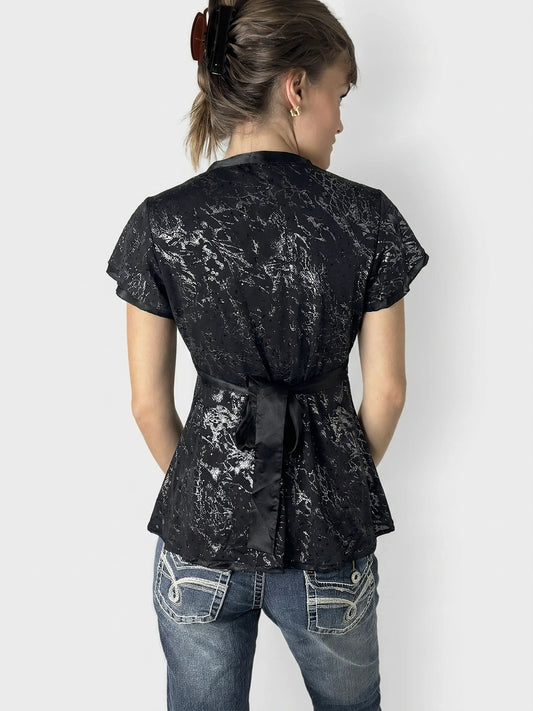 Back view of a black body shirt featuring a floral pattern and a tie at the waist.