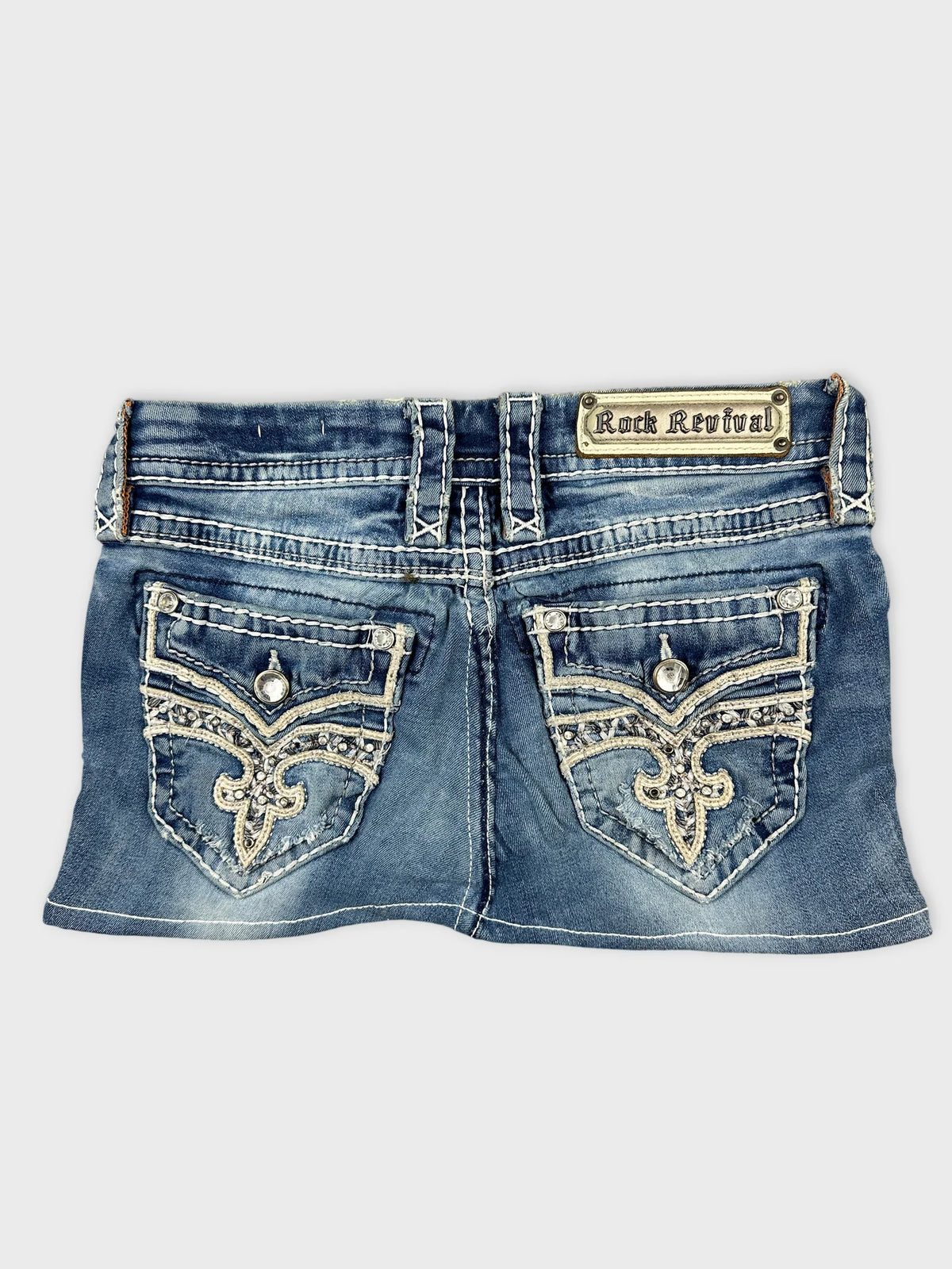 Back view of a blue denim mini skirt with embellished pockets.