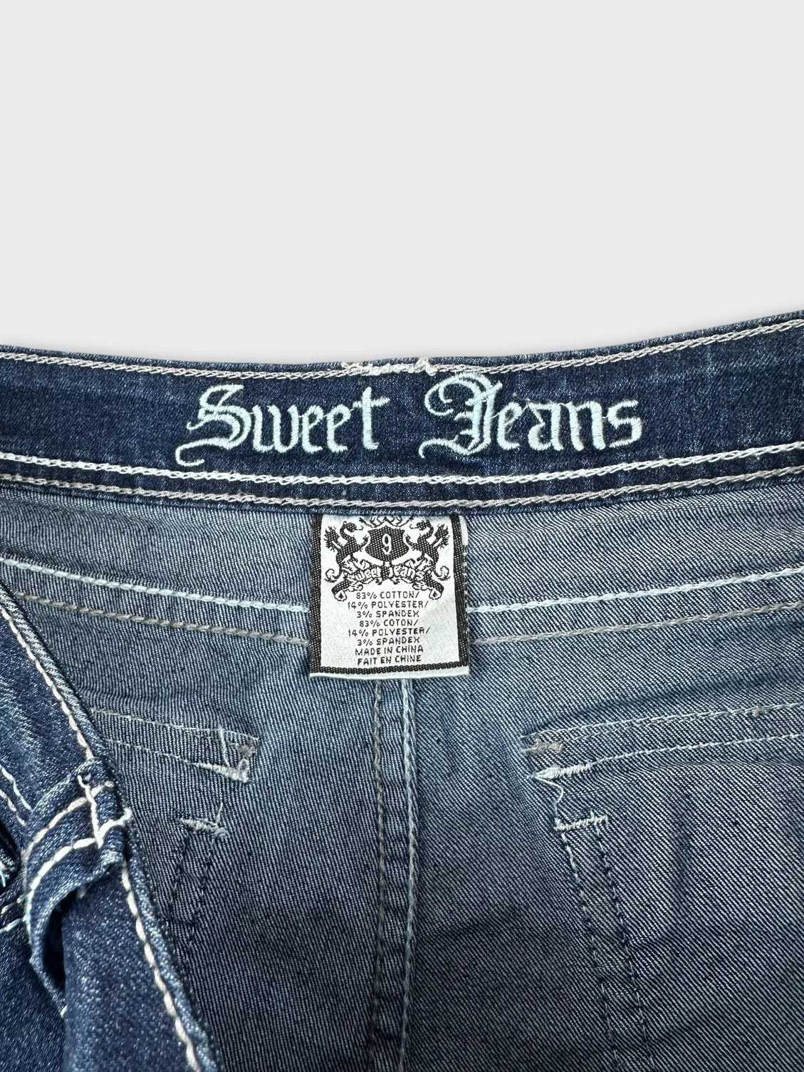 Detail view of blue denim shorts featuring embroidered 'Sweet Jeans' waistband.