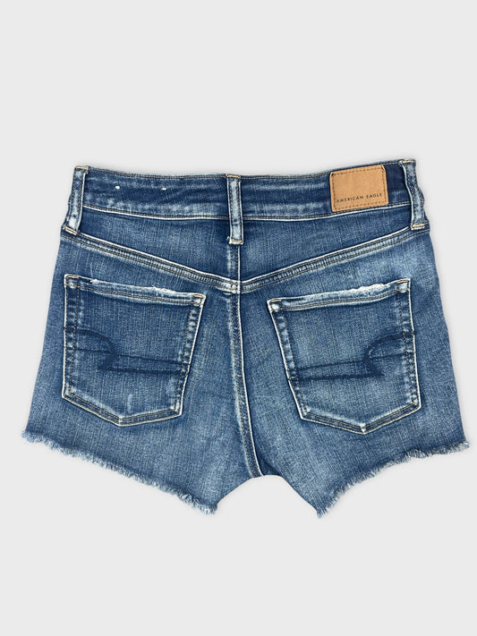 Back view of blue denim shorts featuring frayed hem and two back pockets.