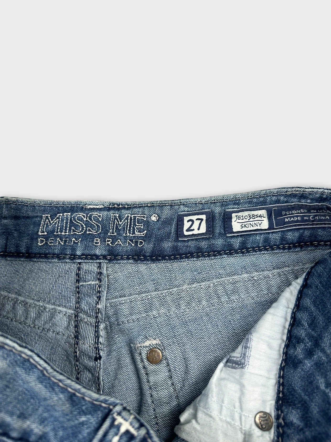 Detail view of a blue denim skirt featuring logo stitching and button closure.