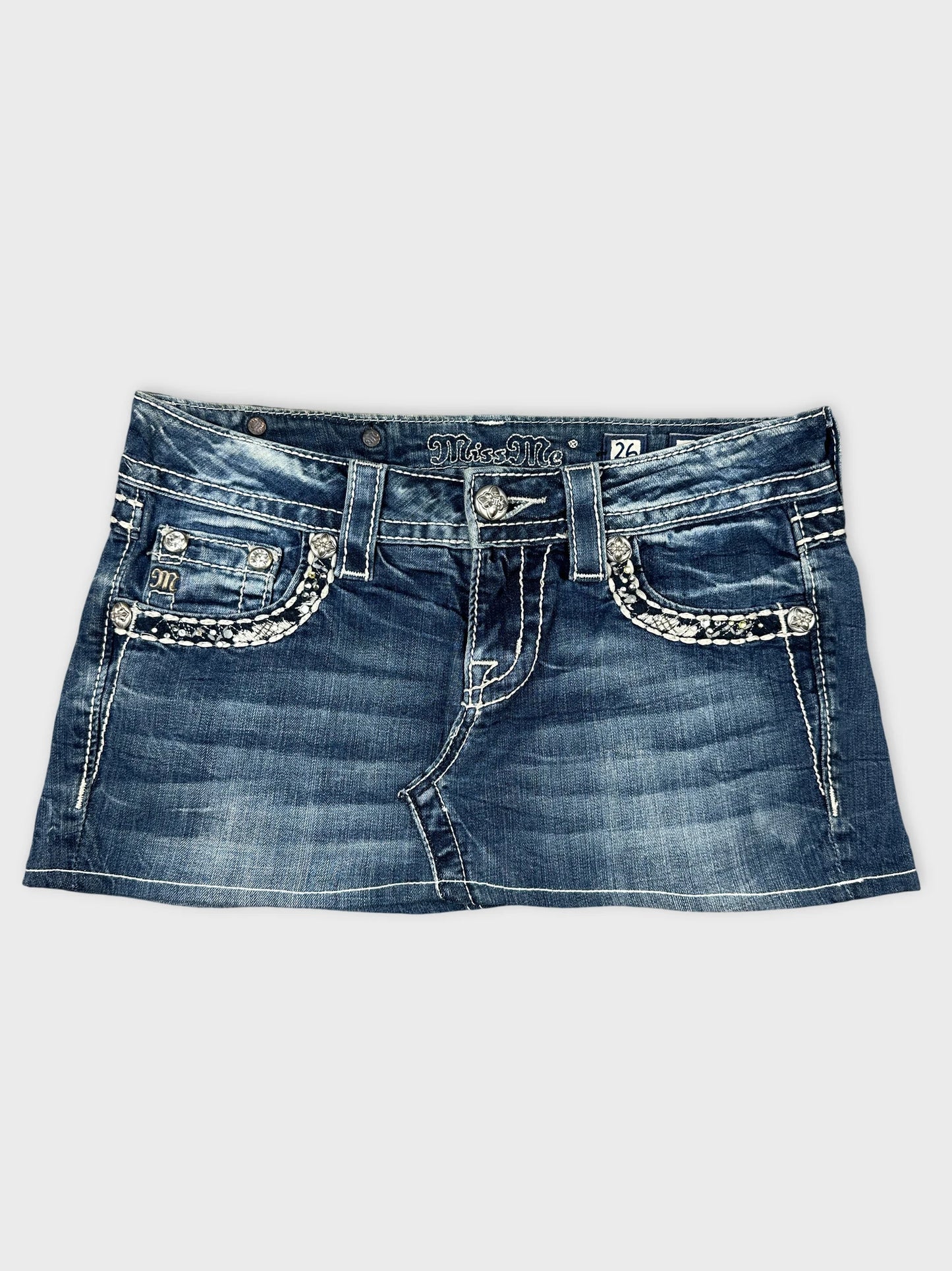 Front view of a denim skirt with silver pocket embellishments.