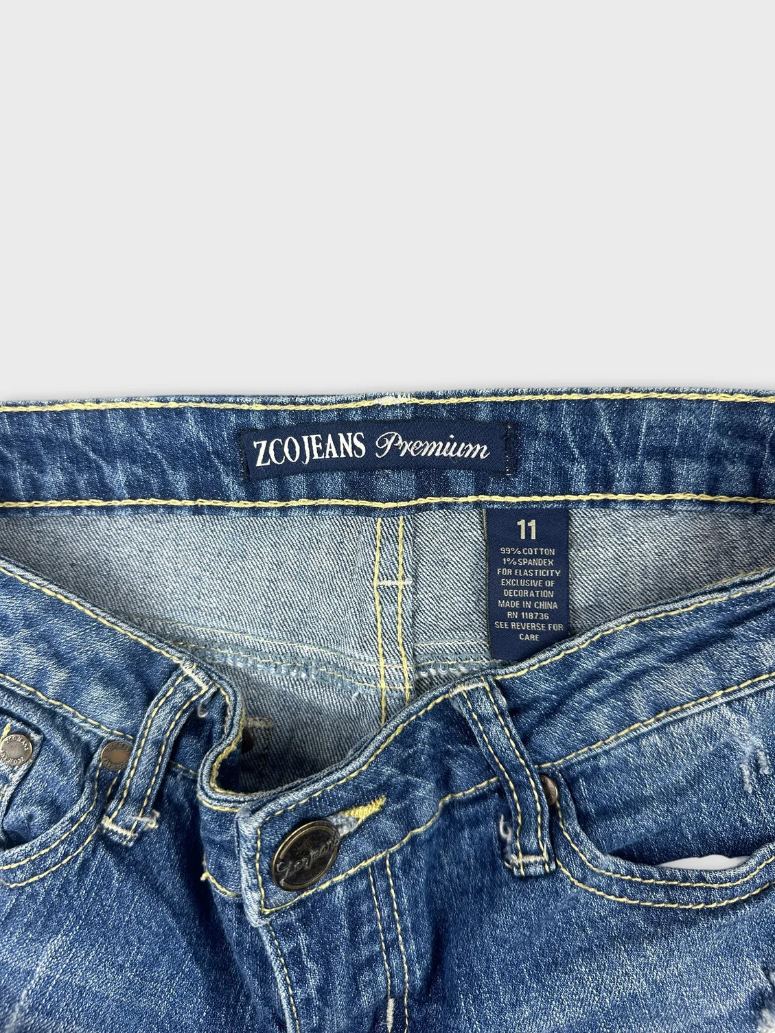 Detail view of blue denim shorts with yellow stitching and button detail.