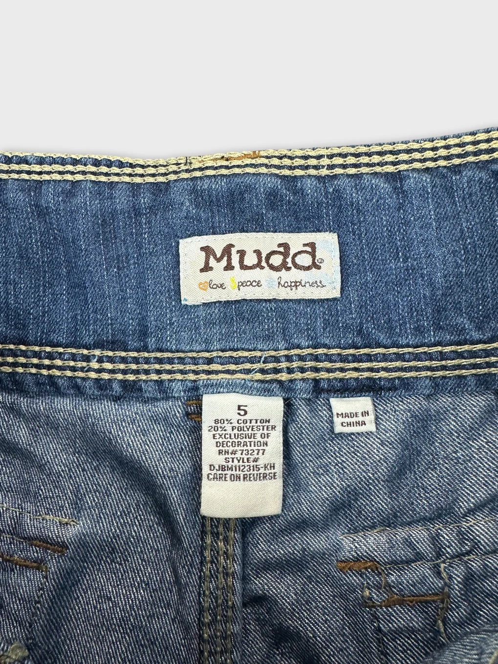 Detail view of blue jeans shorts with Mudd label and yellow stitching.