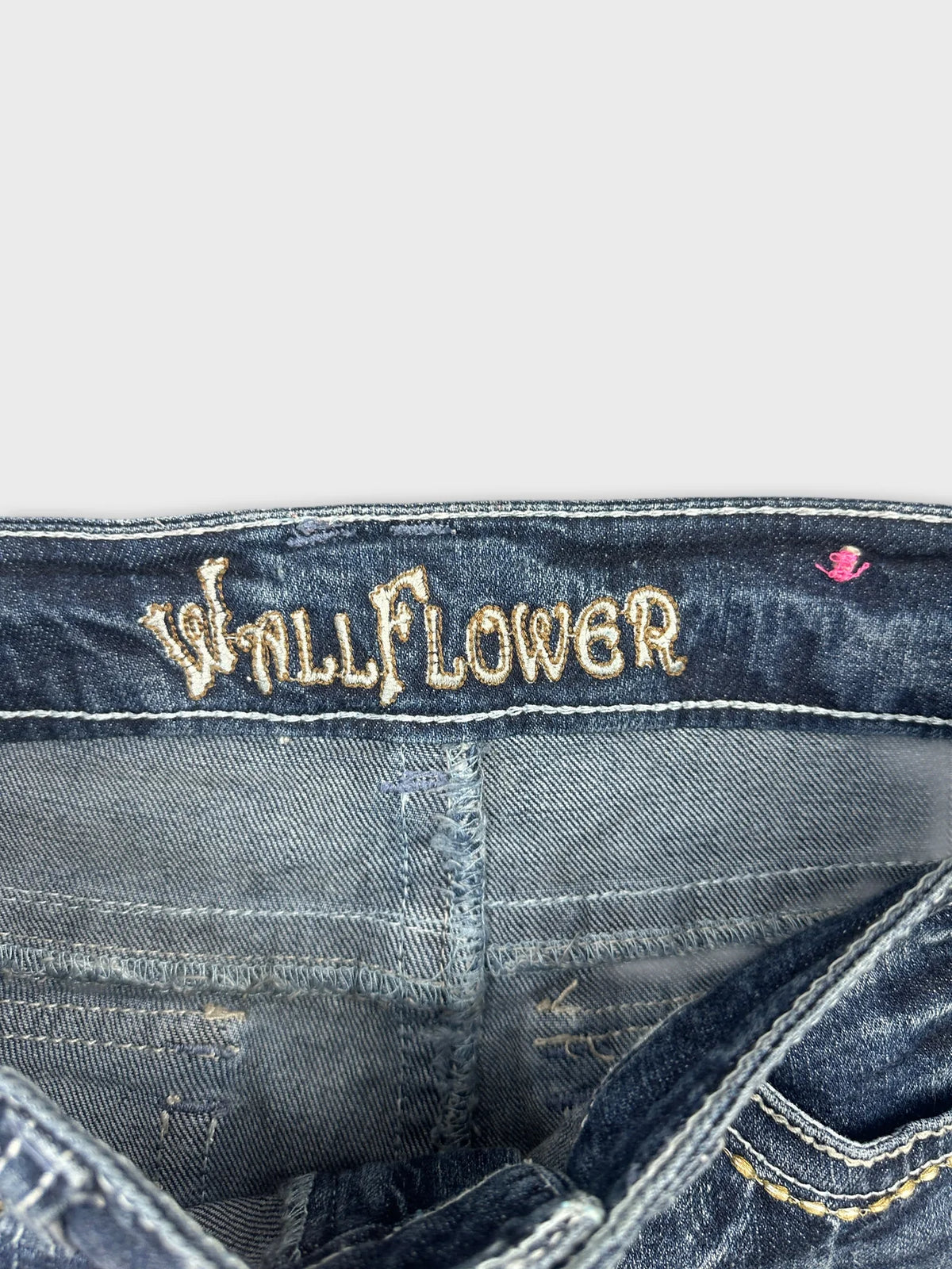 Detail view of blue jeans shorts featuring embroidered 'WallFlower' text.