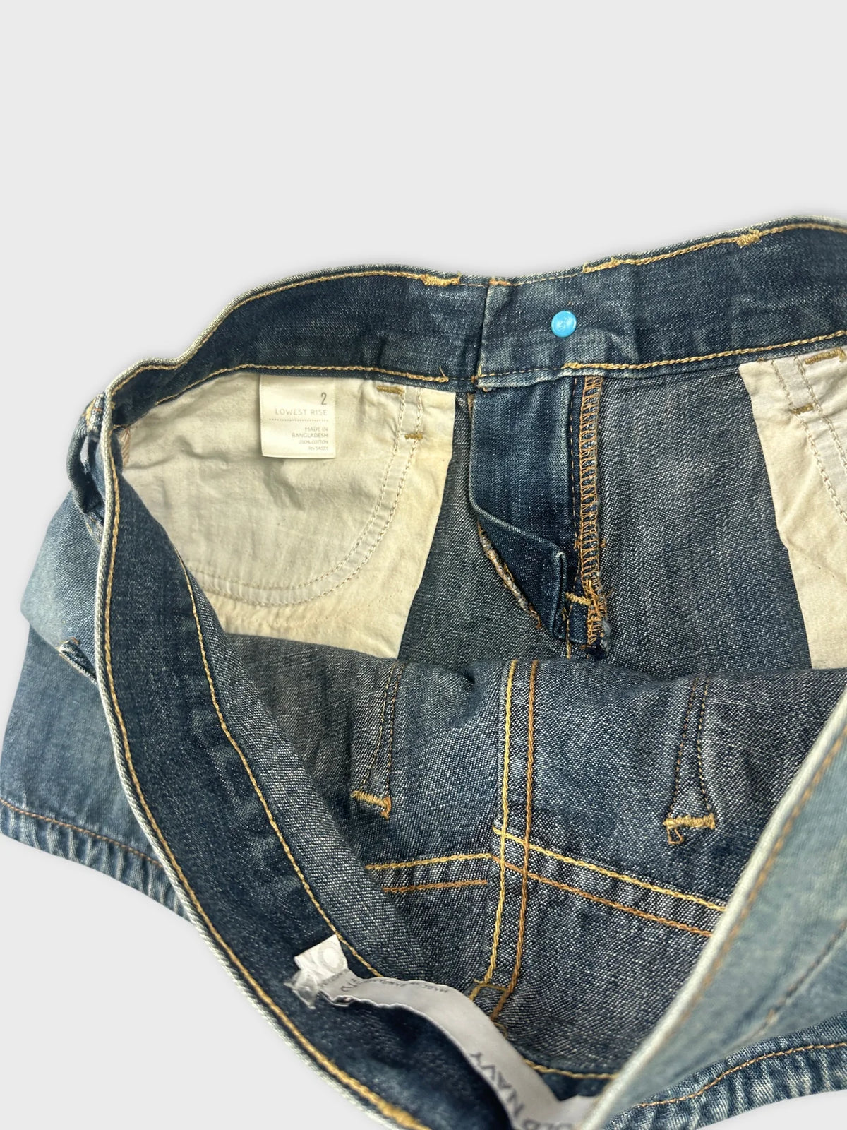 Detail view of women's denim shorts showing blue fabric and yellow stitching.