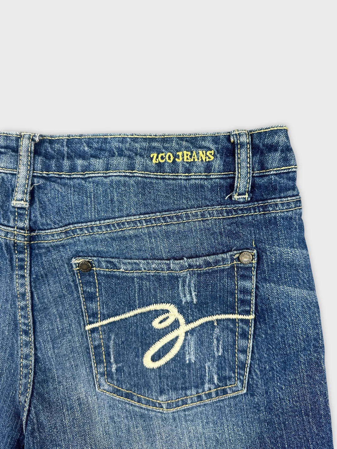 Detail view of blue denim shorts featuring an embroidered design on the back pocket.