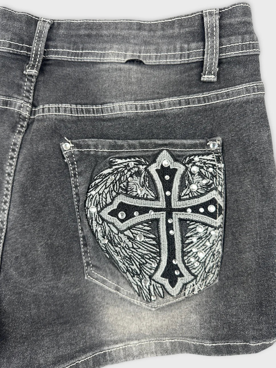 Detail view of black jeans shorts featuring embroidered cross design.