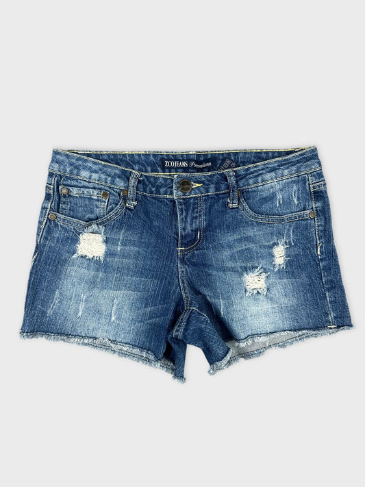 Front view of distressed denim shorts in blue with frayed hem.