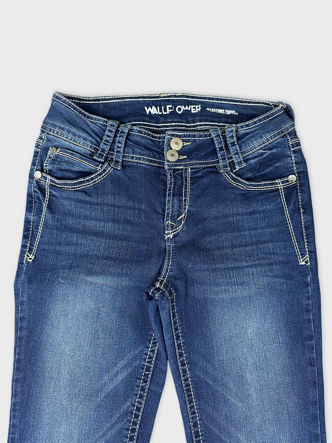 Detail view of blue jeans featuring contrasting white stitching and dual button closure.