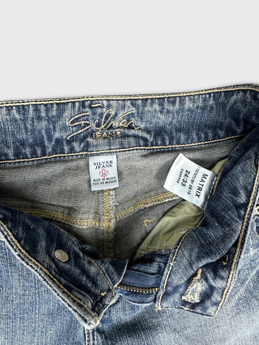 Detail view of blue denim jeans featuring Silver Jeans branding and zipper.