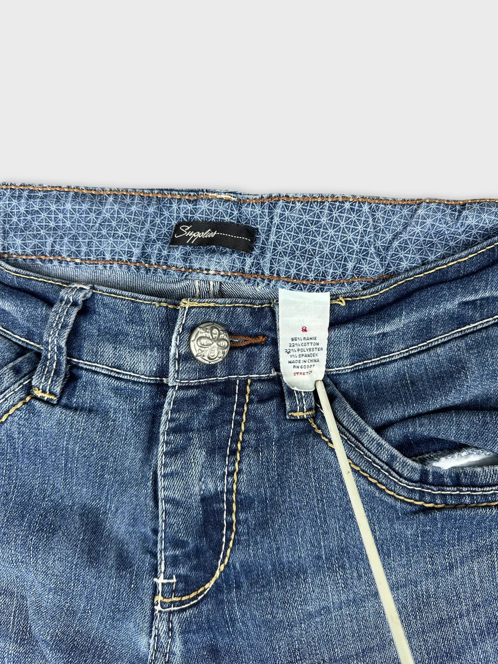 Detail view of blue long jeans with waistband and logo tag.