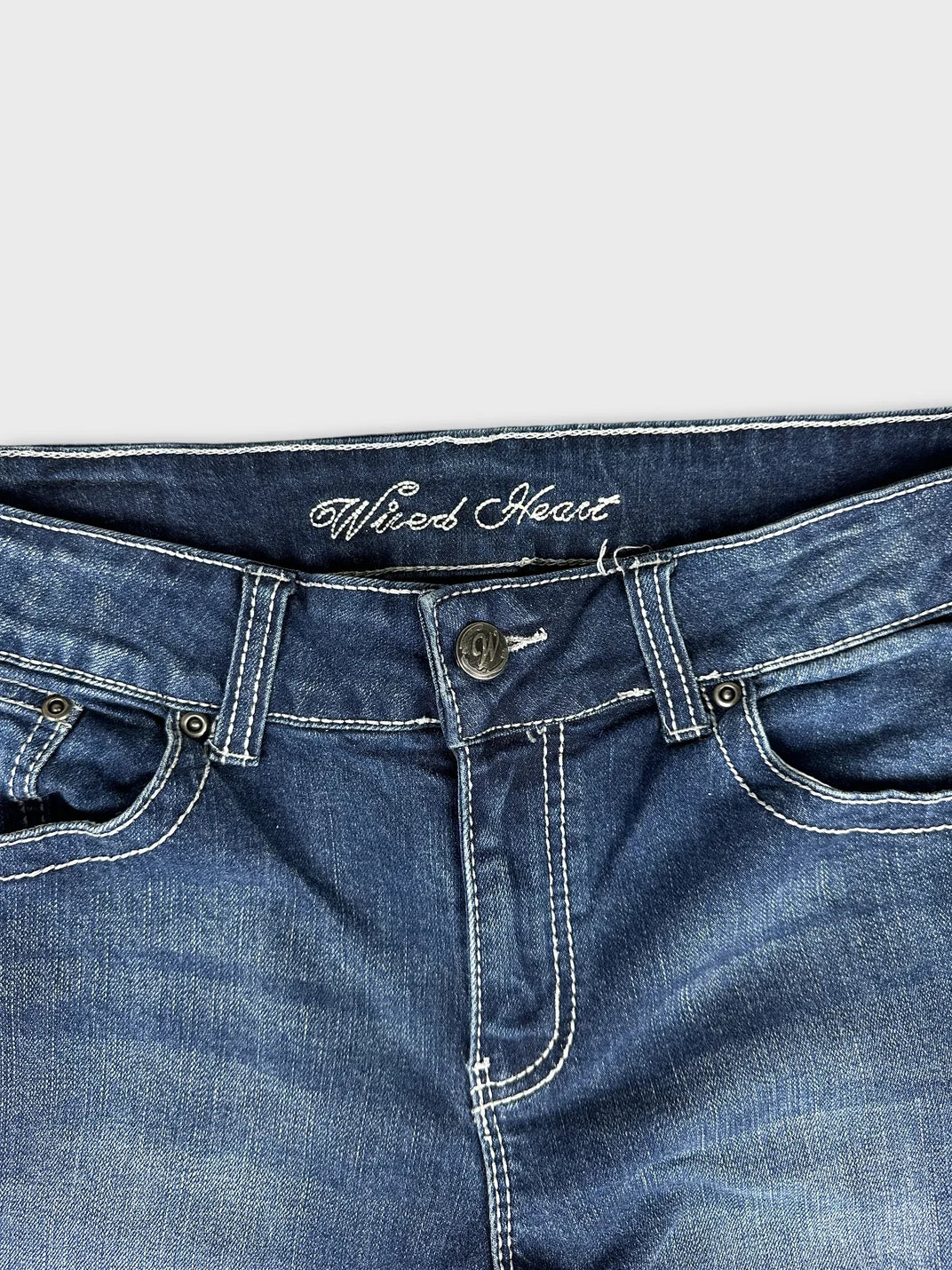 Detail view of dark blue denim jeans with white stitching and button