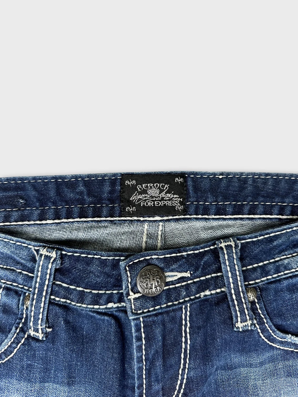 Detail view of women's long jeans featuring a dark blue color and button.