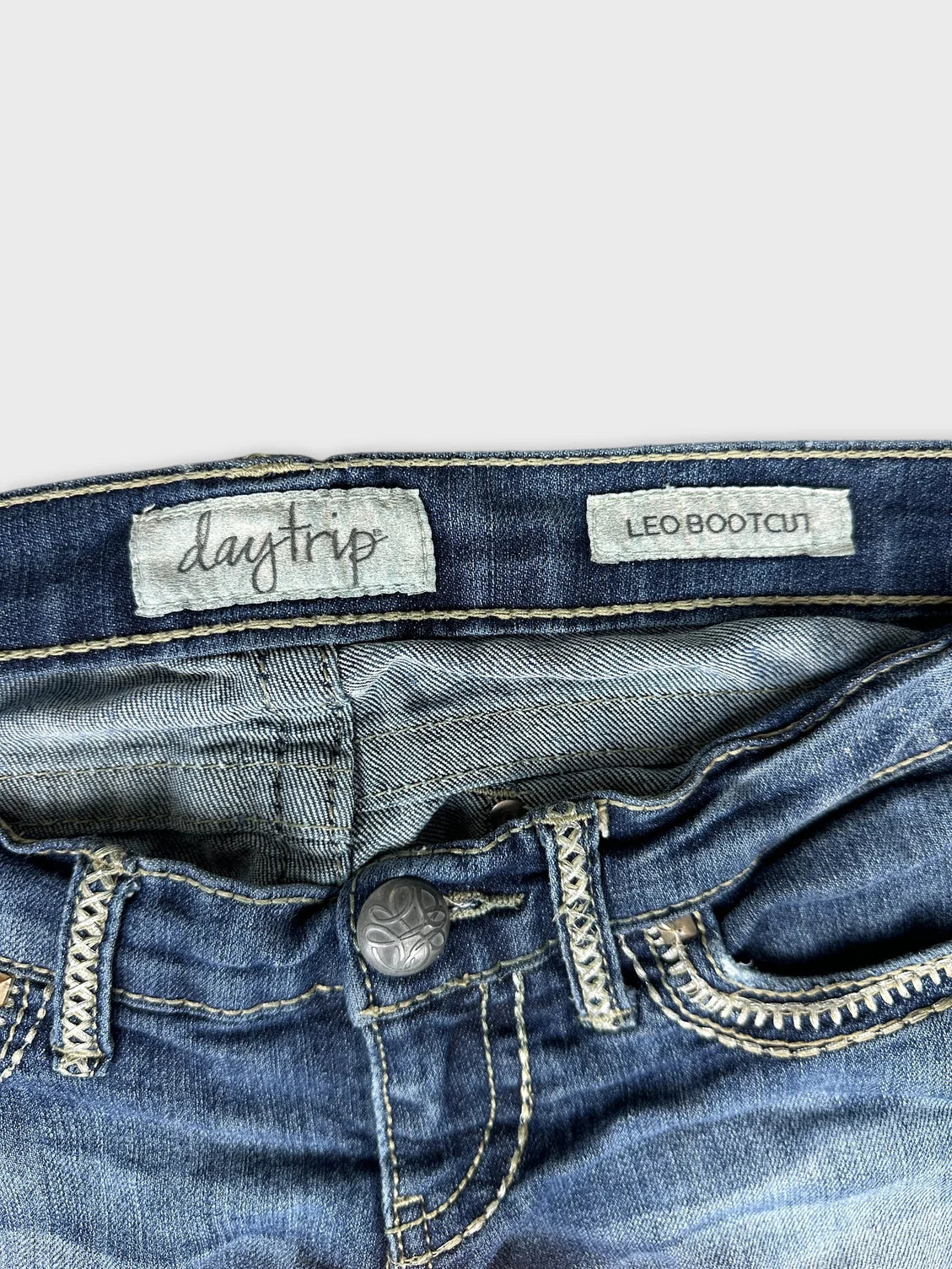 Detail view of blue bootcut jeans featuring decorative stitching and a button.