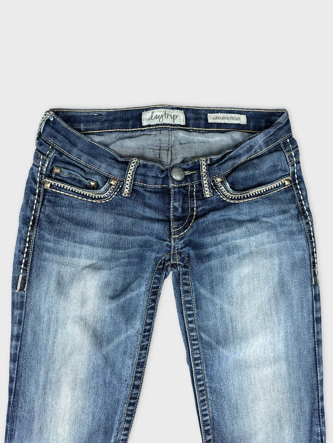 Detail view of blue denim jeans featuring decorative stitching and pocket design.