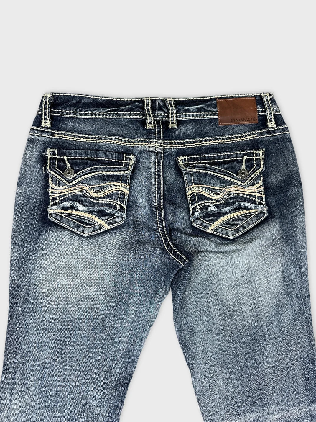 Detail view of long jeans in dark blue with patterned back pockets.