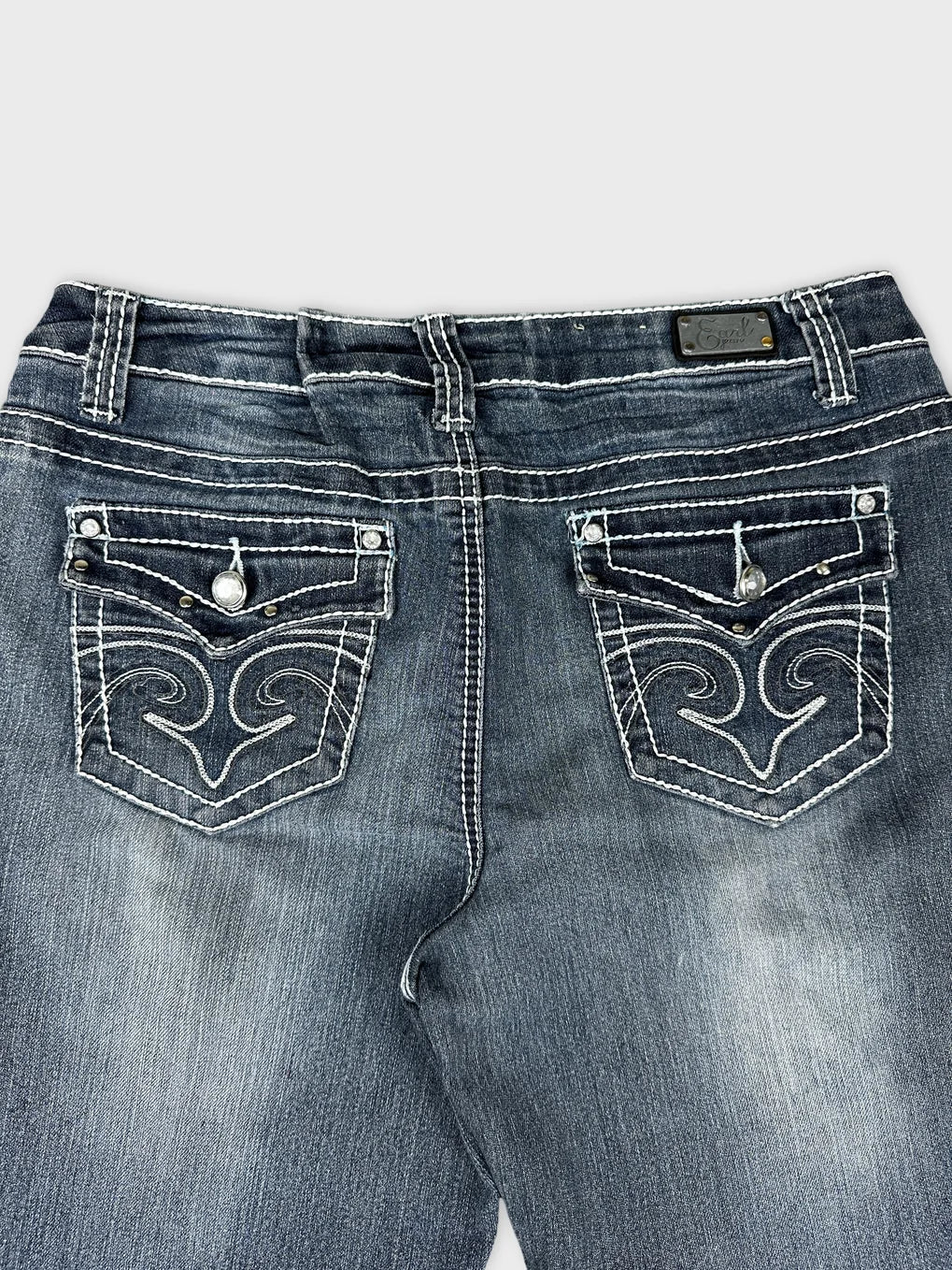 Detail view of women’s long jeans in dark blue with decorative back pockets.