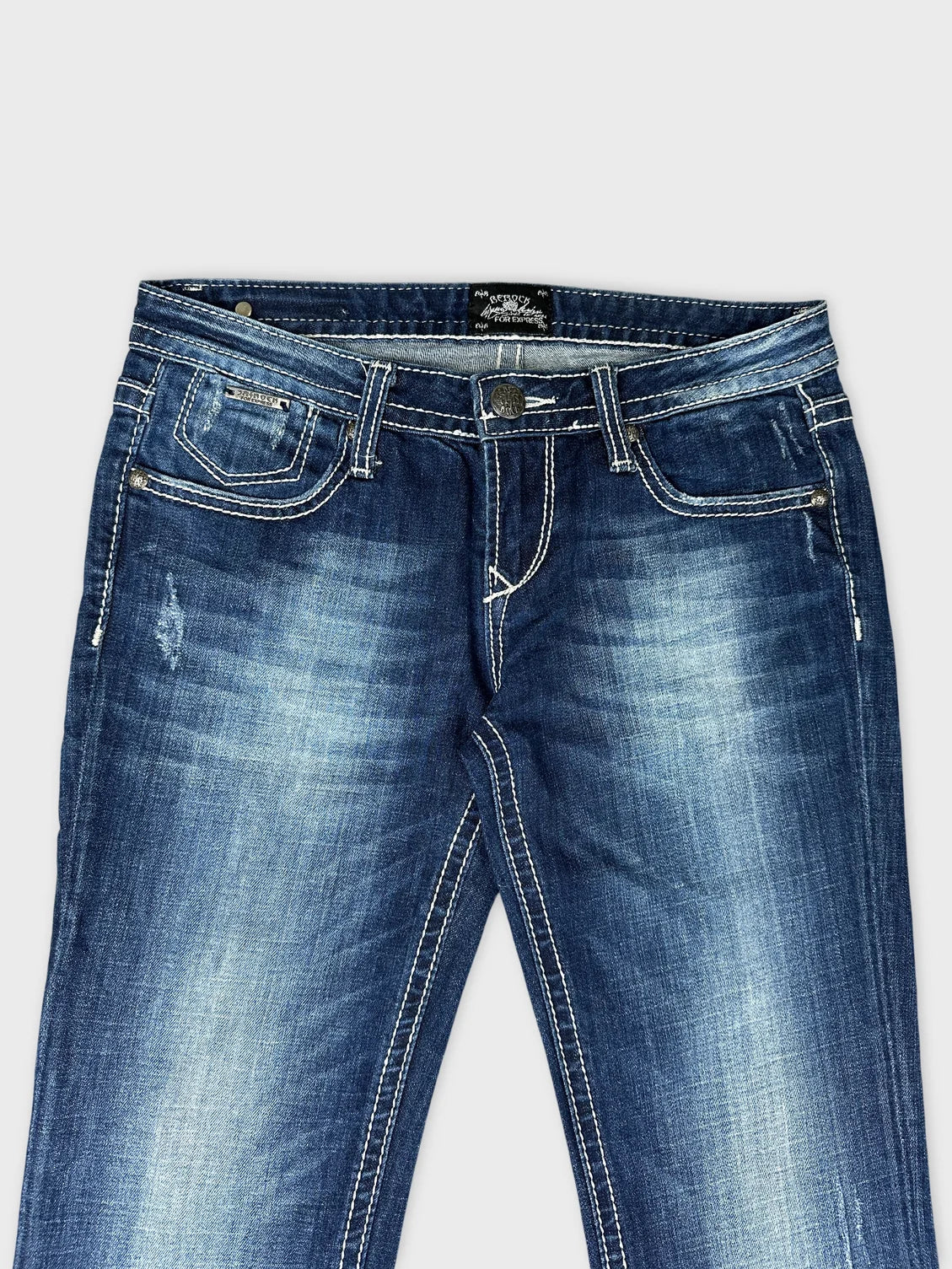 Detail view of women’s long jeans in dark blue with contrasting white stitching.