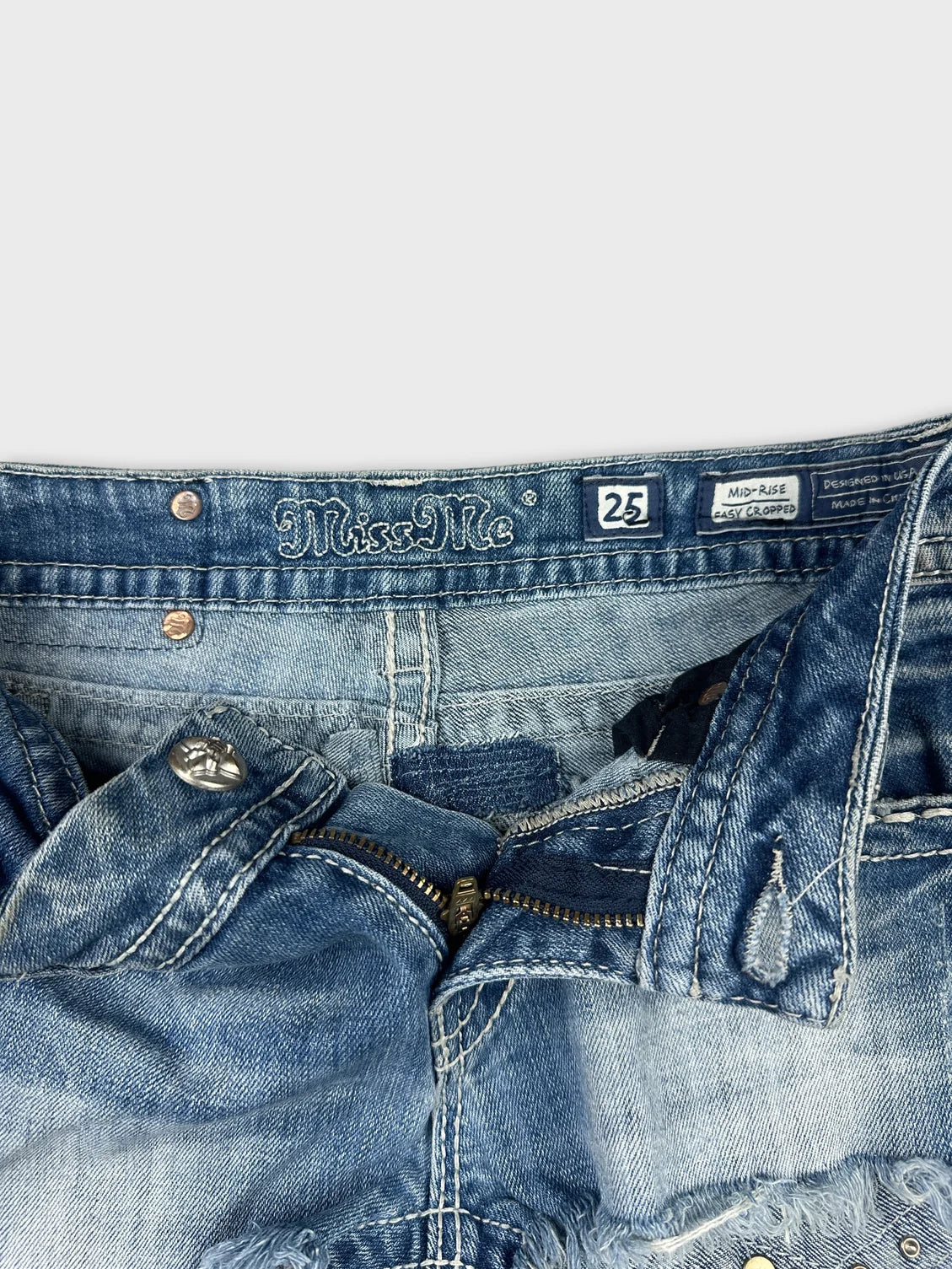Detail view of blue denim mini shorts with zipper and button details.