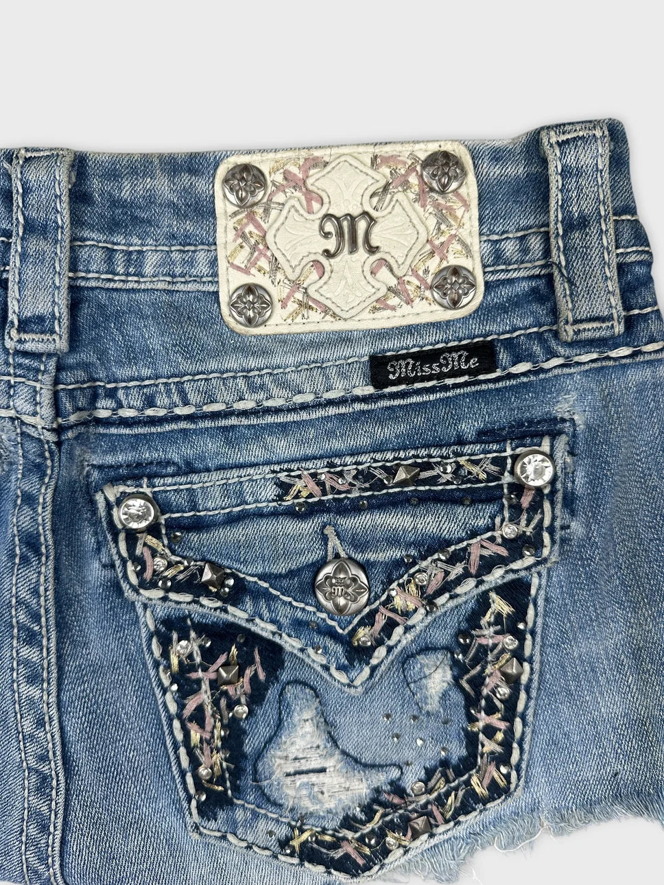 Detail view of blue denim mini shorts featuring embellished back pockets.