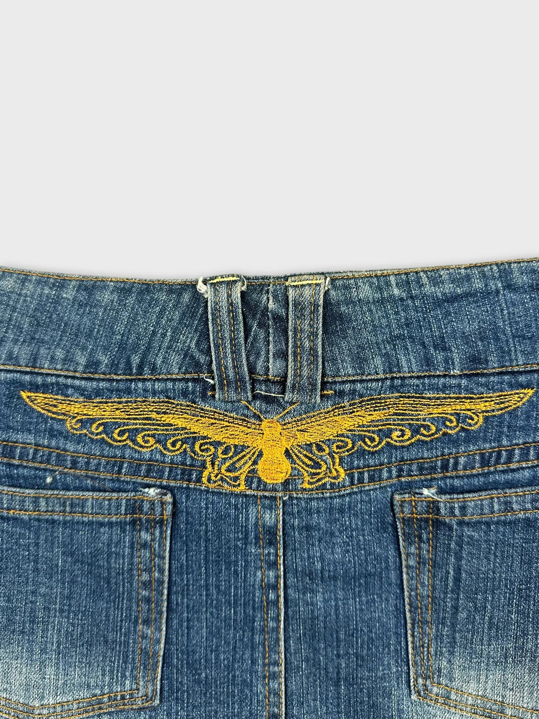 Detail view of a denim miniskirt featuring yellow embroidered design on the back.