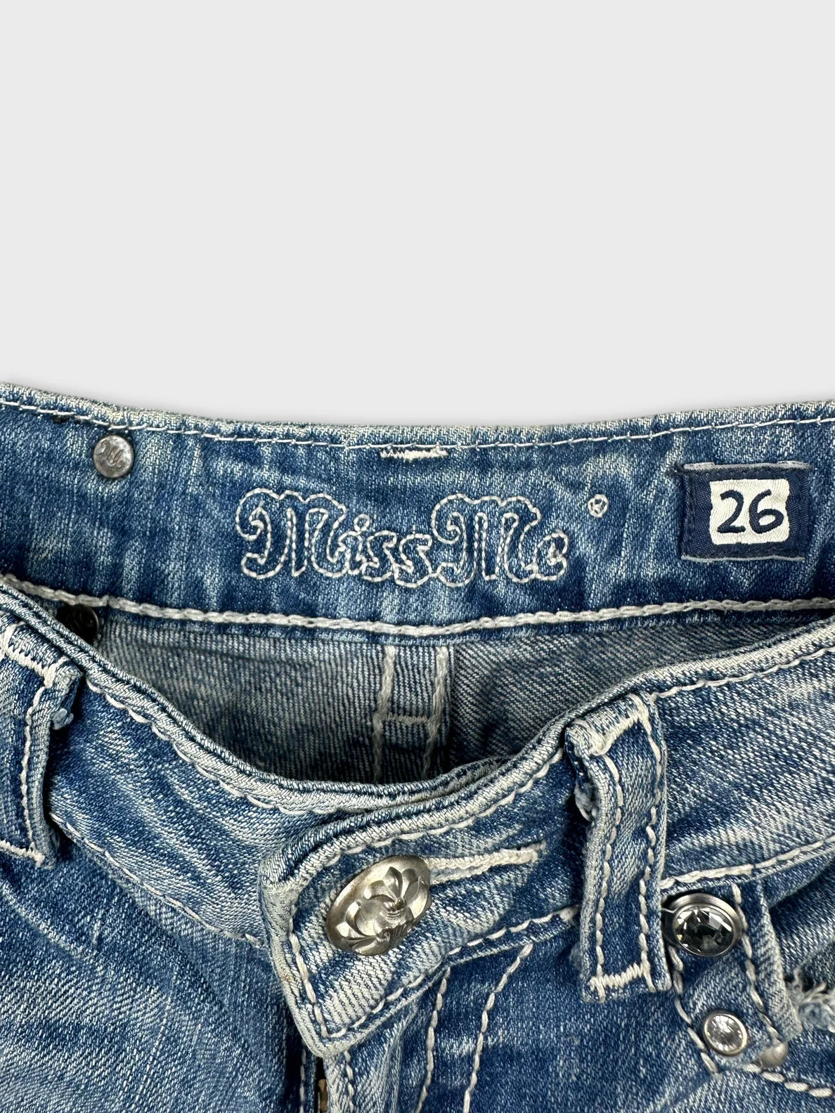 Detail view of denim shorts showing blue fabric and decorative metal button.