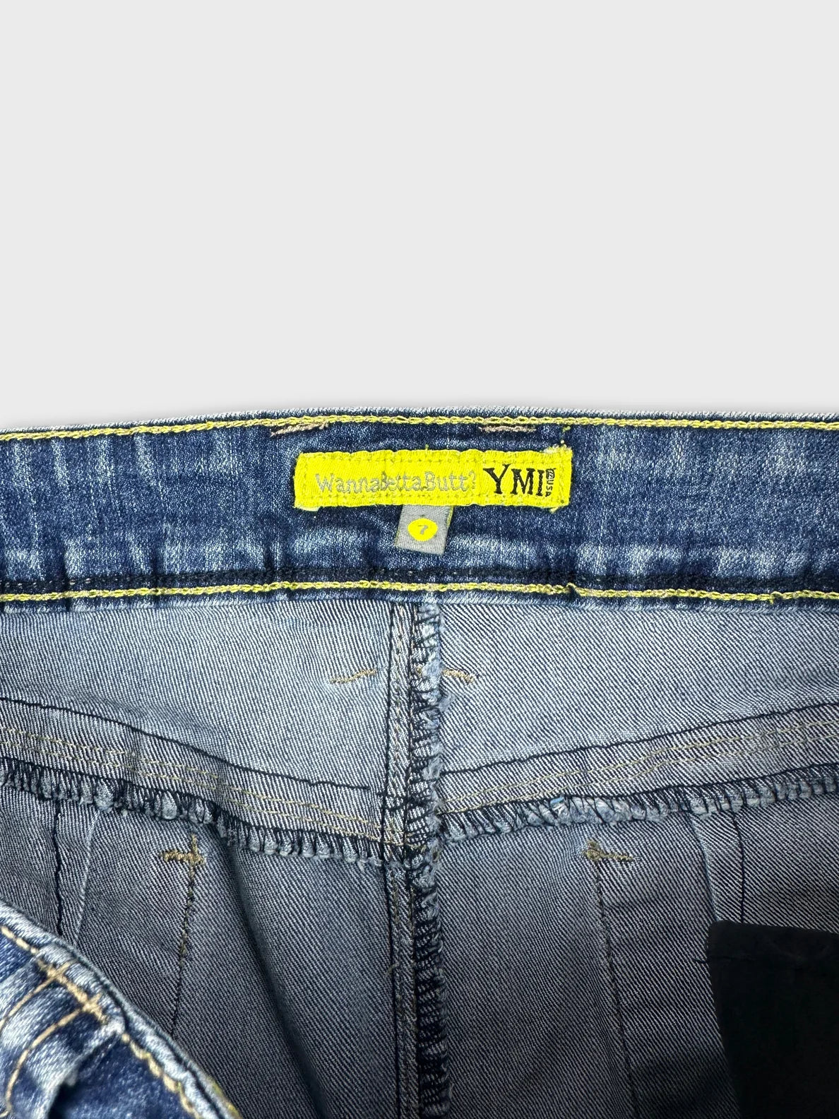 Detail view of blue denim shorts with yellow trim and label.