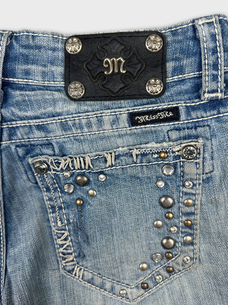 Detail view of blue denim shorts featuring studded embellishments and logo patch.