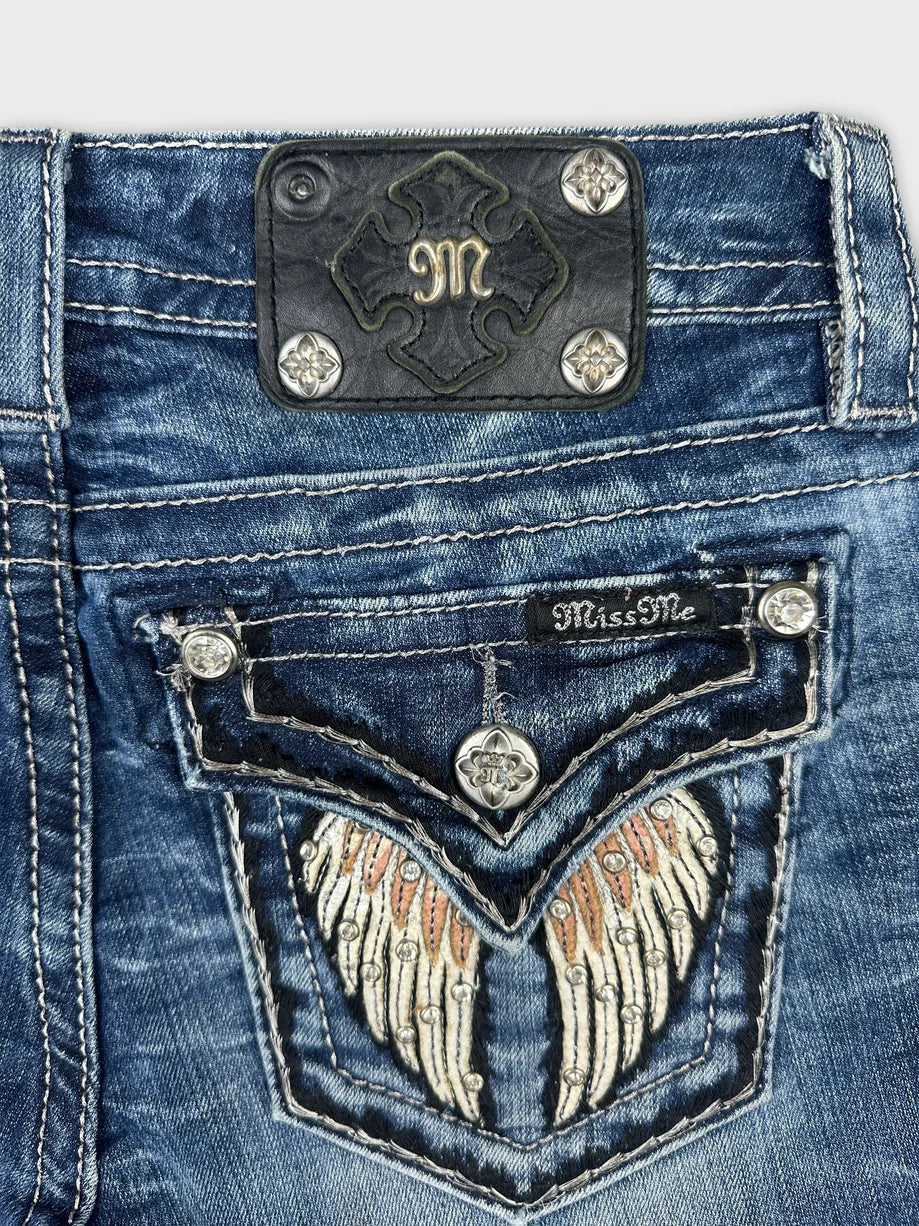 Detail view of blue denim shorts featuring embroidered wing design and metal studs.