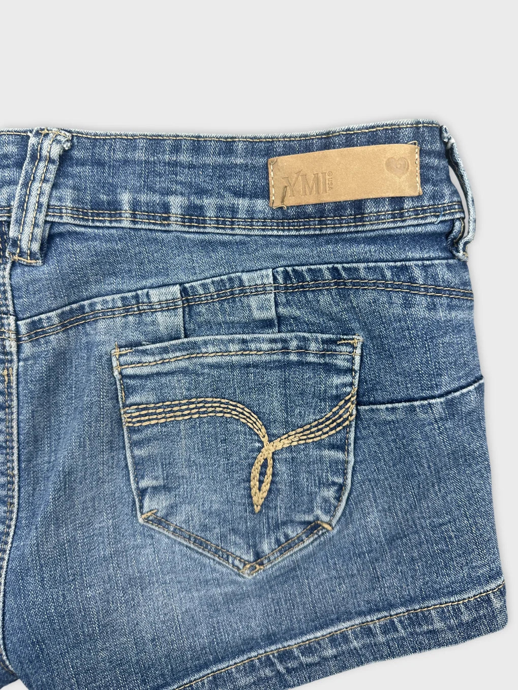 Detail view of blue denim shorts with decorative stitching on back pocket.