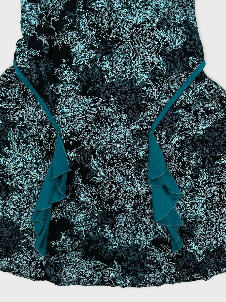 Detail view of a black floral skirt with teal ruffle trim.