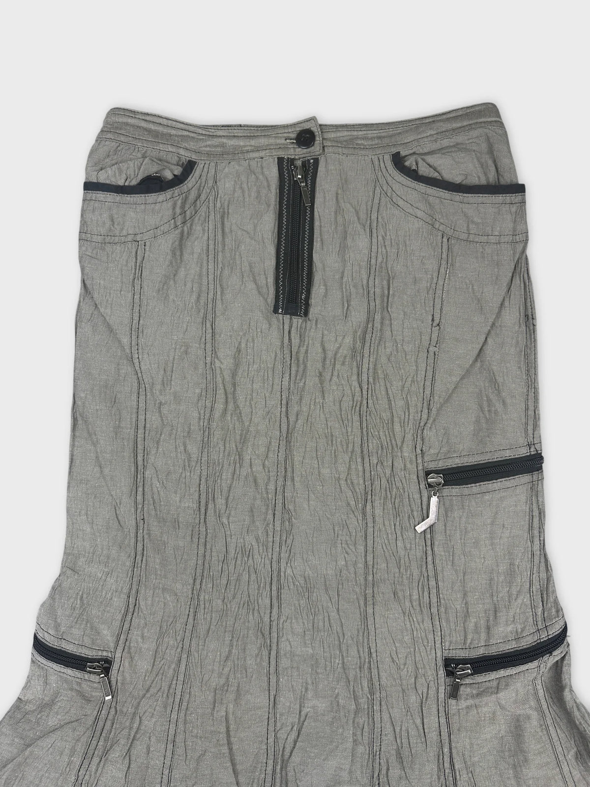 Detail view of a gray skirt featuring zippered pockets and pleated texture.