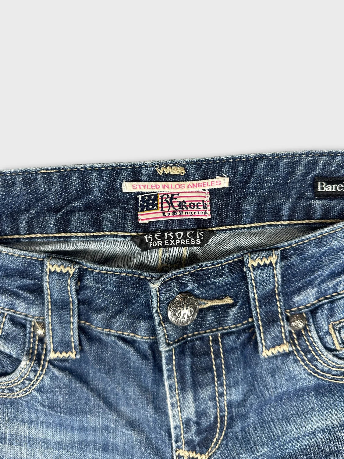 Detail view of blue denim jeans featuring a silver button and logo tag.