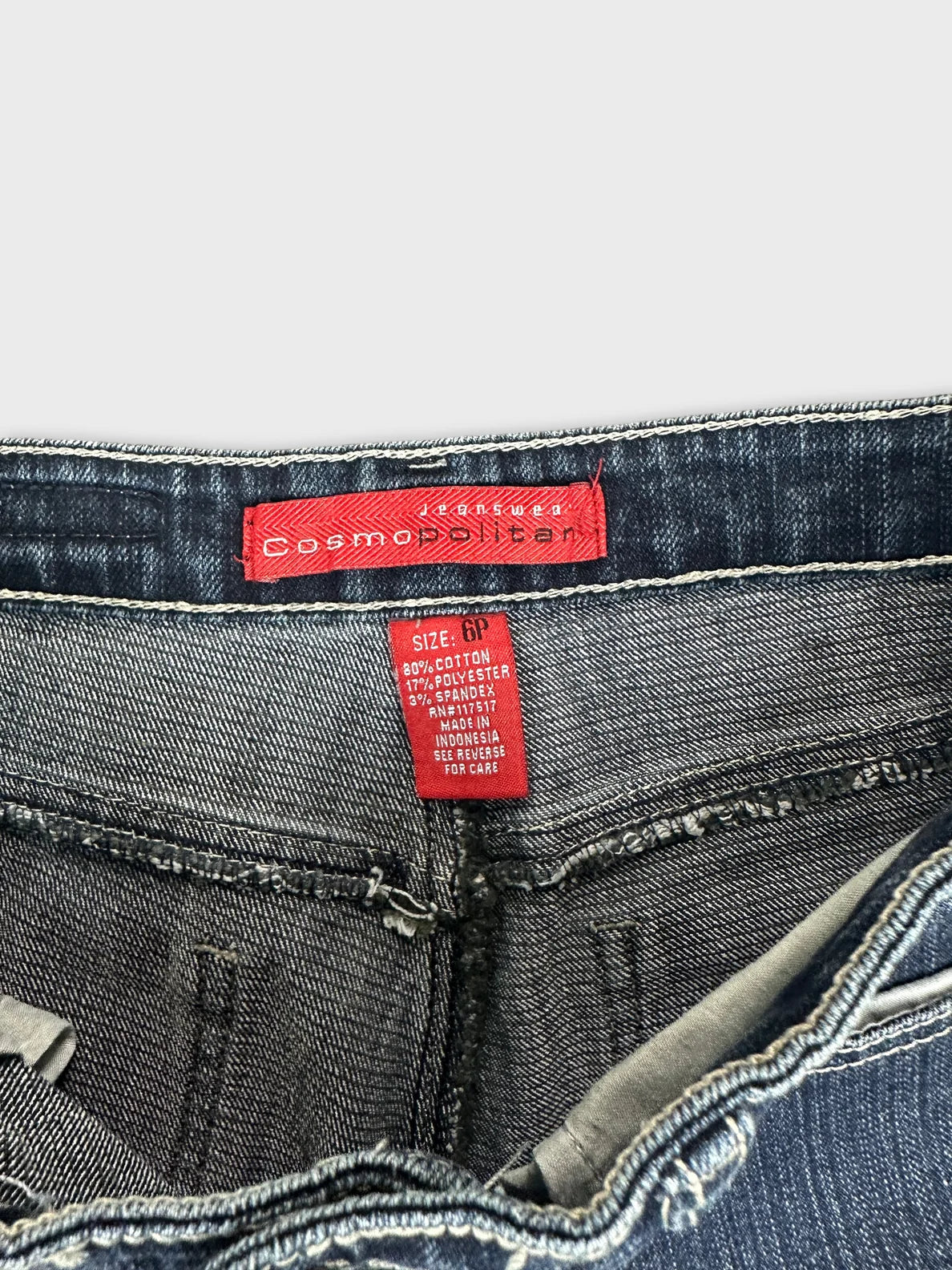 Detail view of dark blue denim jeans featuring red tag and stitching.