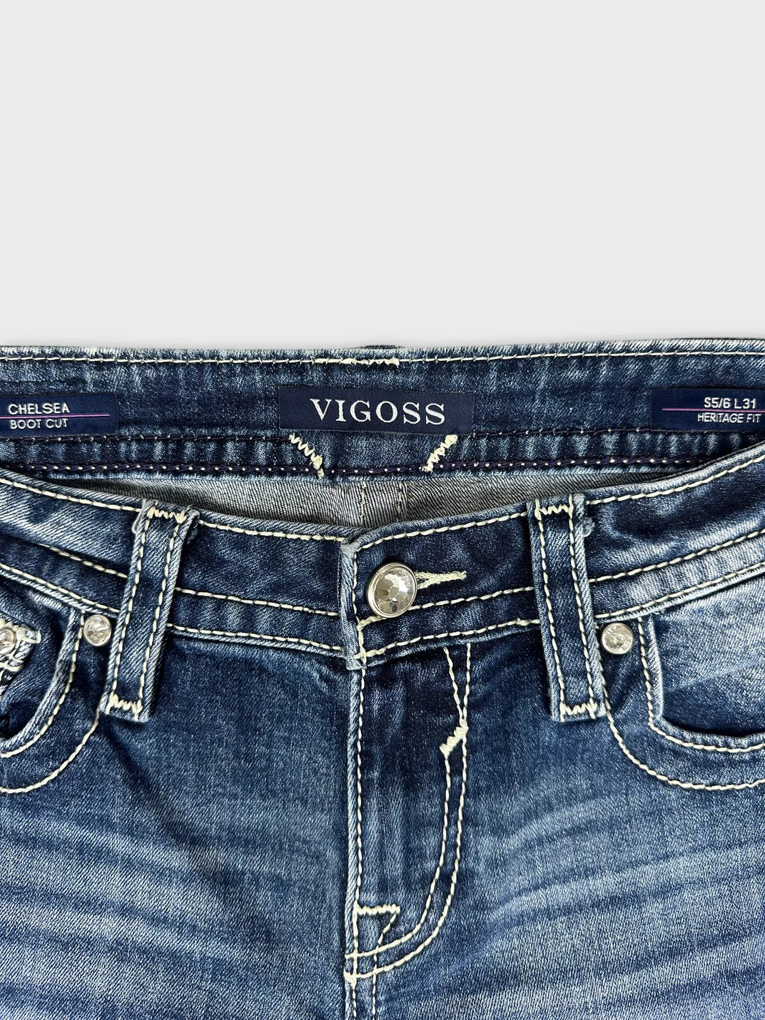 Detail view of dark blue denim jeans featuring visible stitching and a button closure.