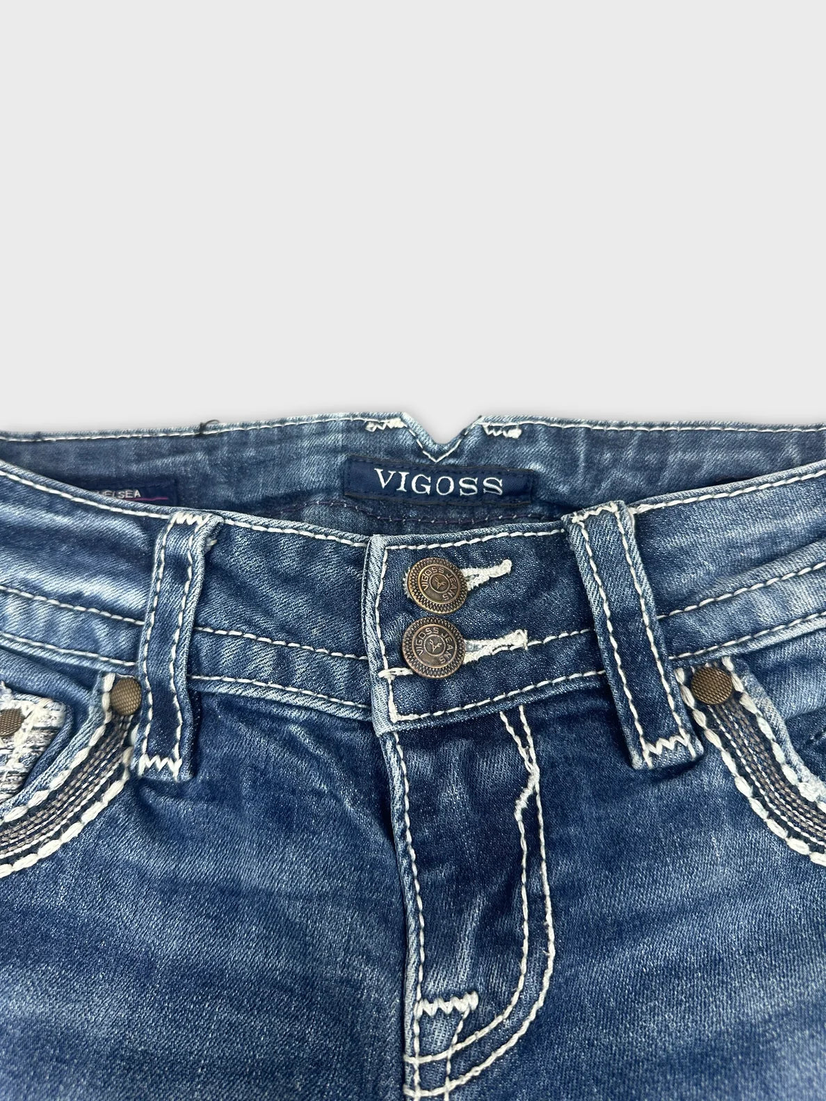 Detail view of blue denim jeans featuring a decorative button design.