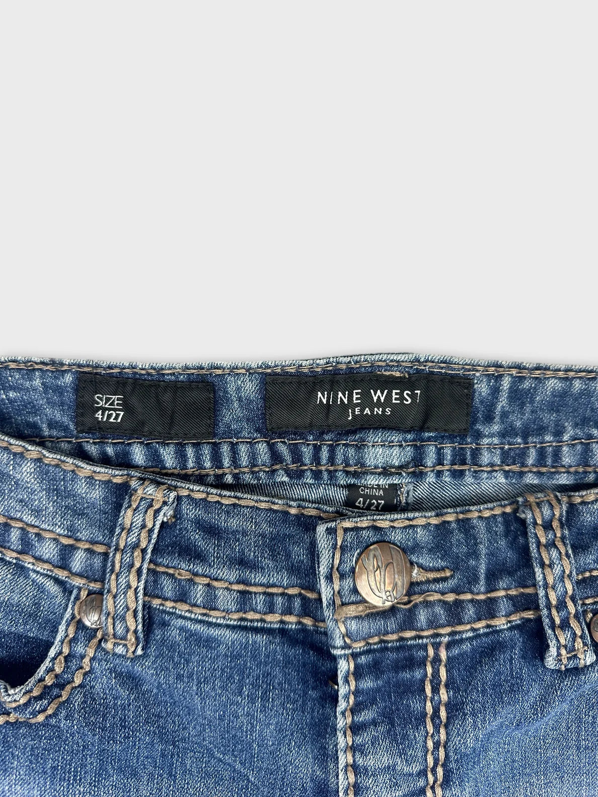 Detail view of women denim jeans in blue with stitched trim and button closure.