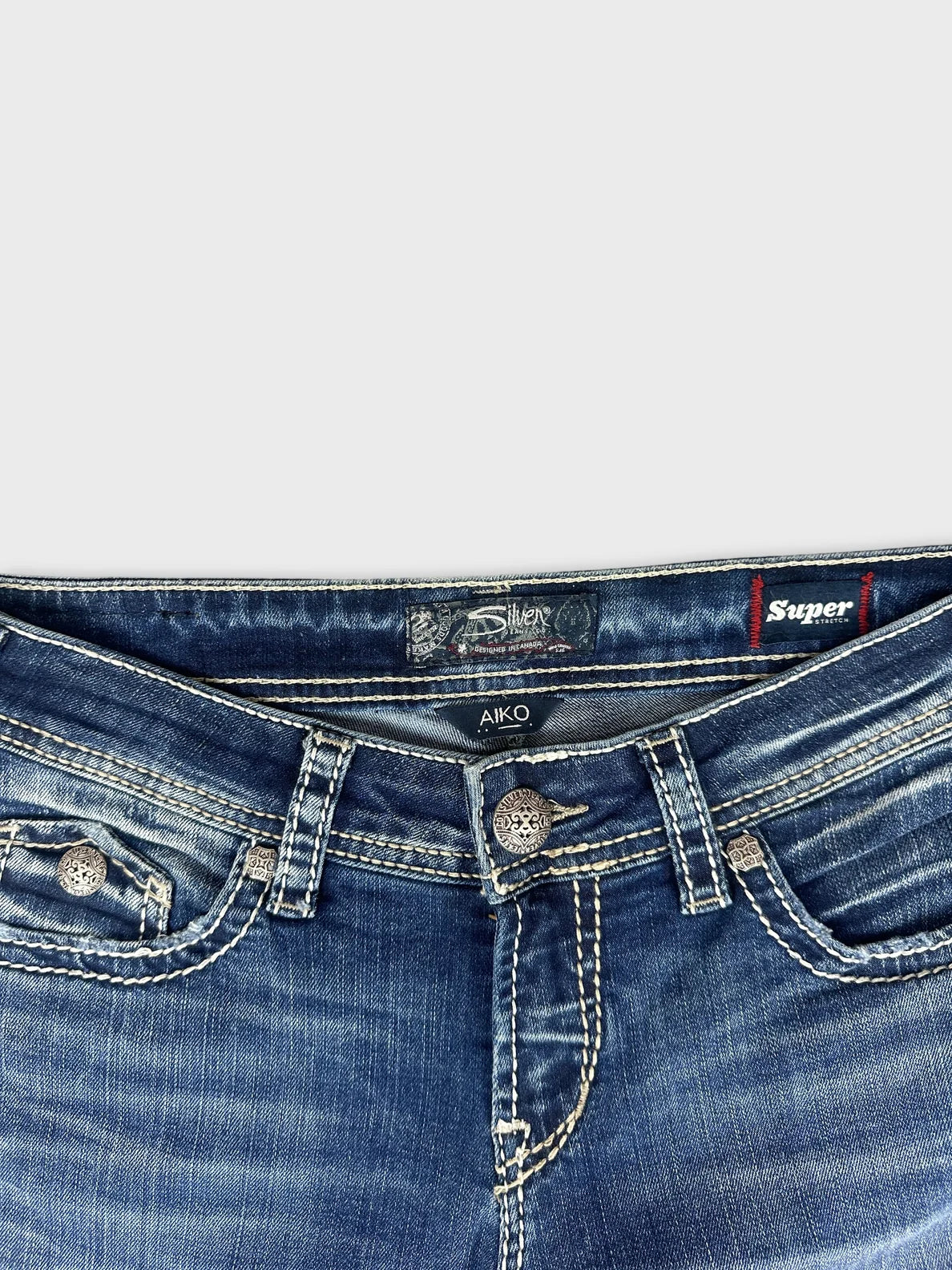 Detail view of blue denim jeans featuring decorative pockets and stitched trim.