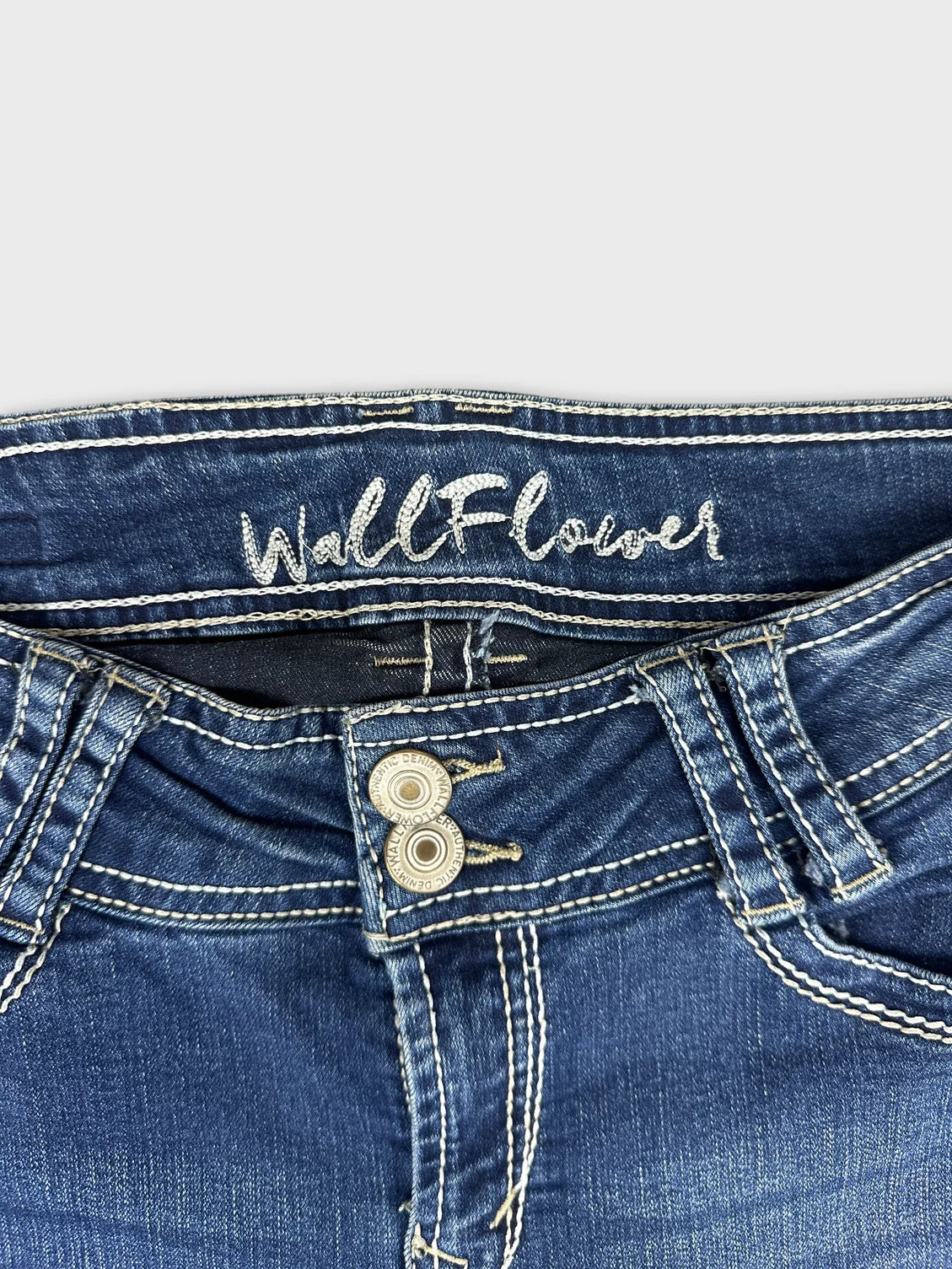 Detail view of women denim jeans in dark blue with visible button and stitching.