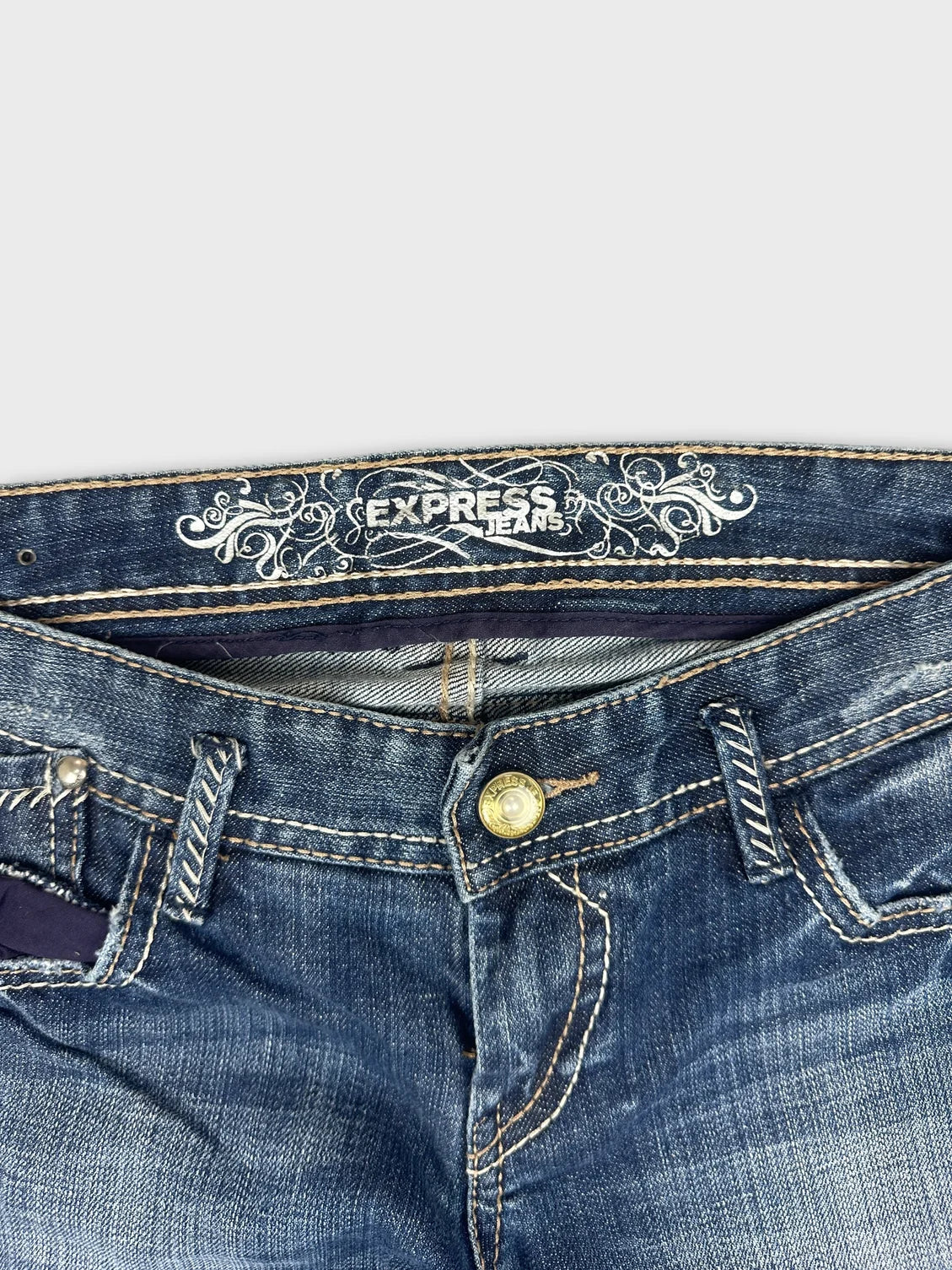 Detail view of blue denim jeans showcasing embroidered waistband and gold button.