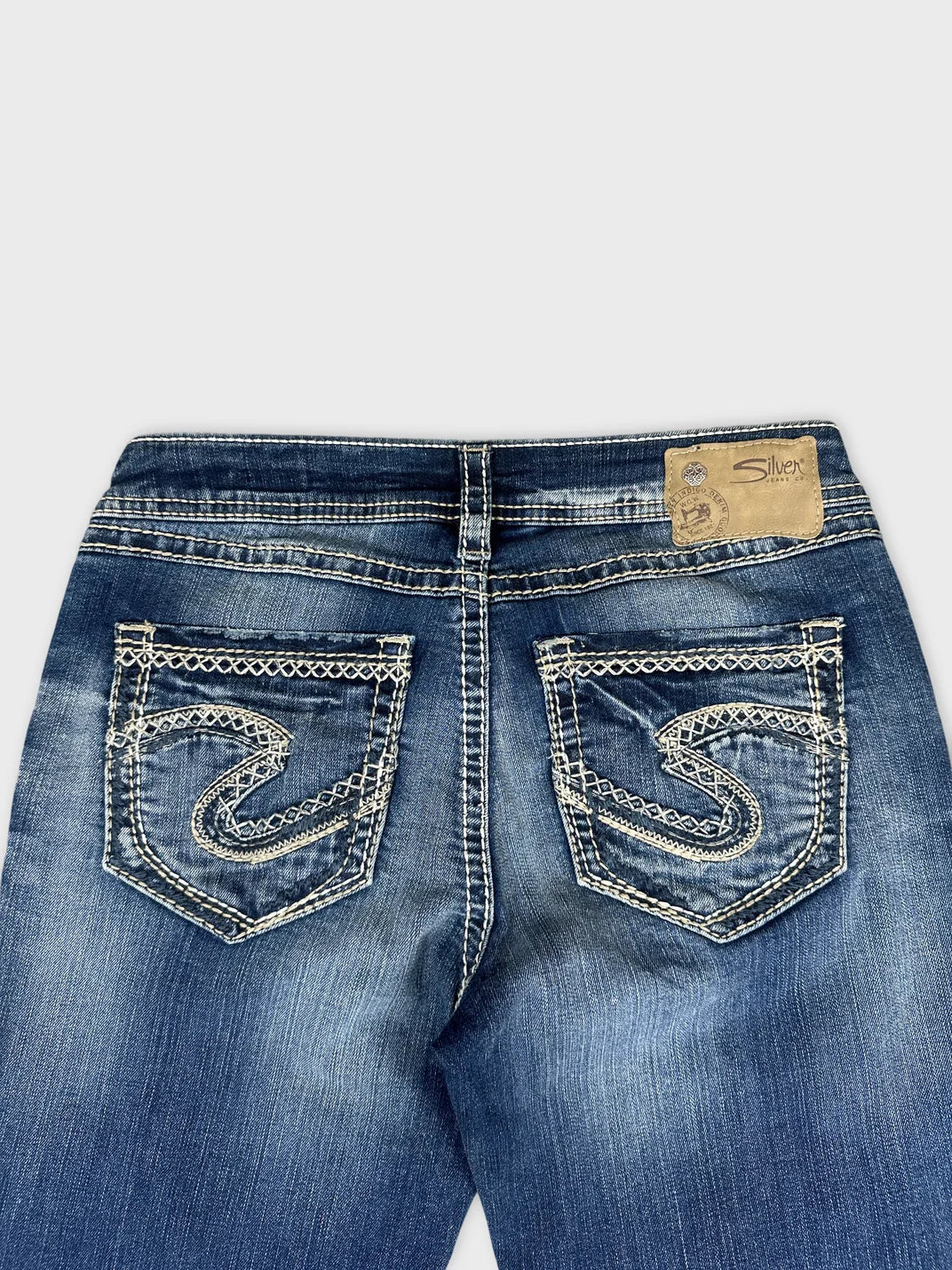 Detail view of women's denim jeans in dark blue with decorative stitching on pockets.