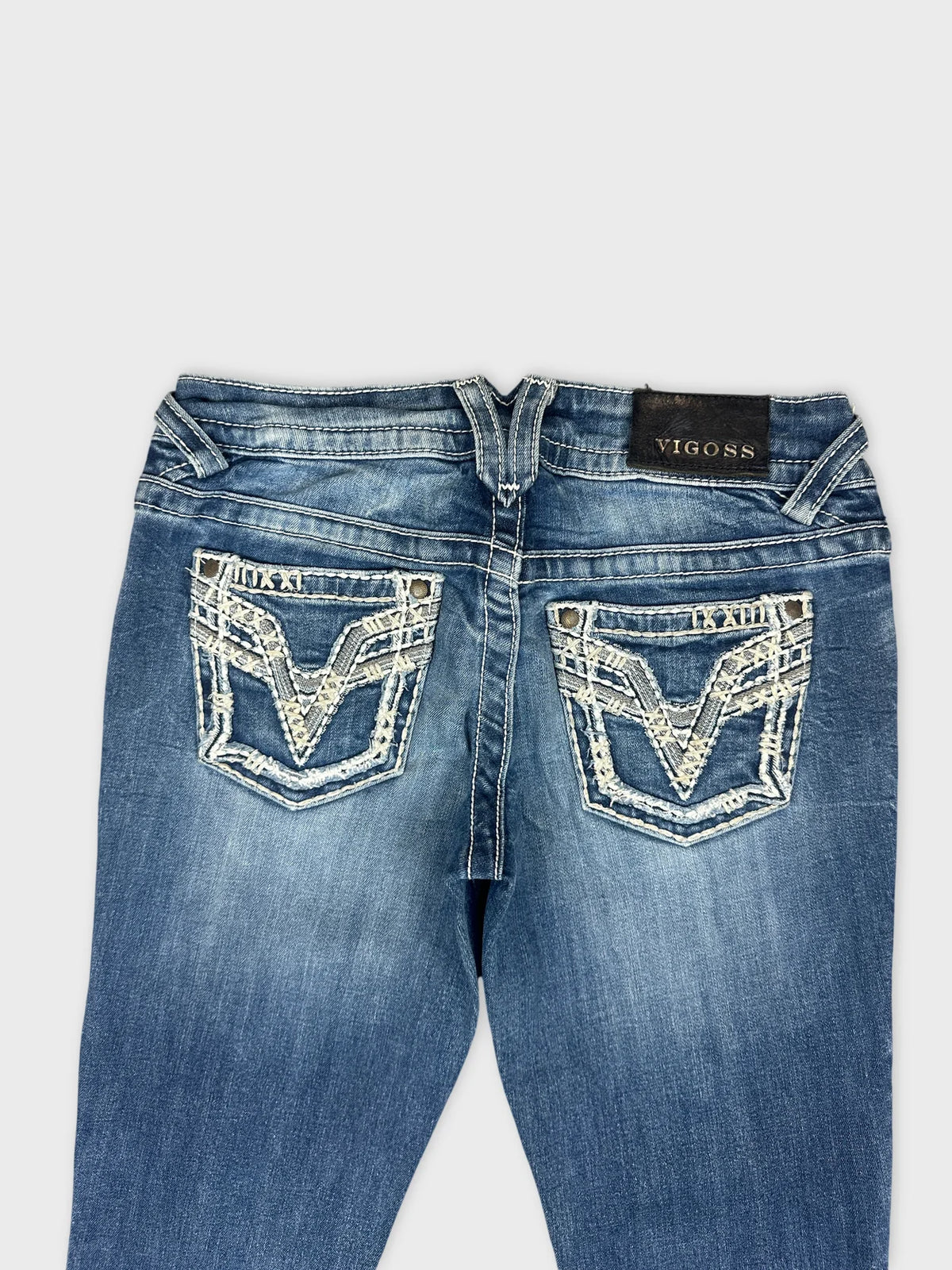 Detail view of blue denim jeans featuring decorative stitching on back pockets.