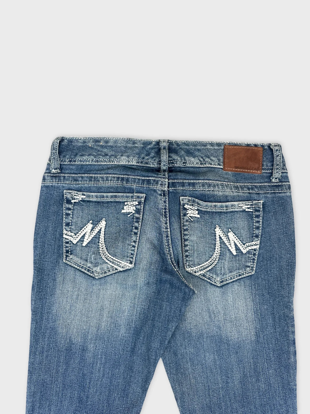 Detail view of blue denim jeans featuring decorative stitching on back pockets.