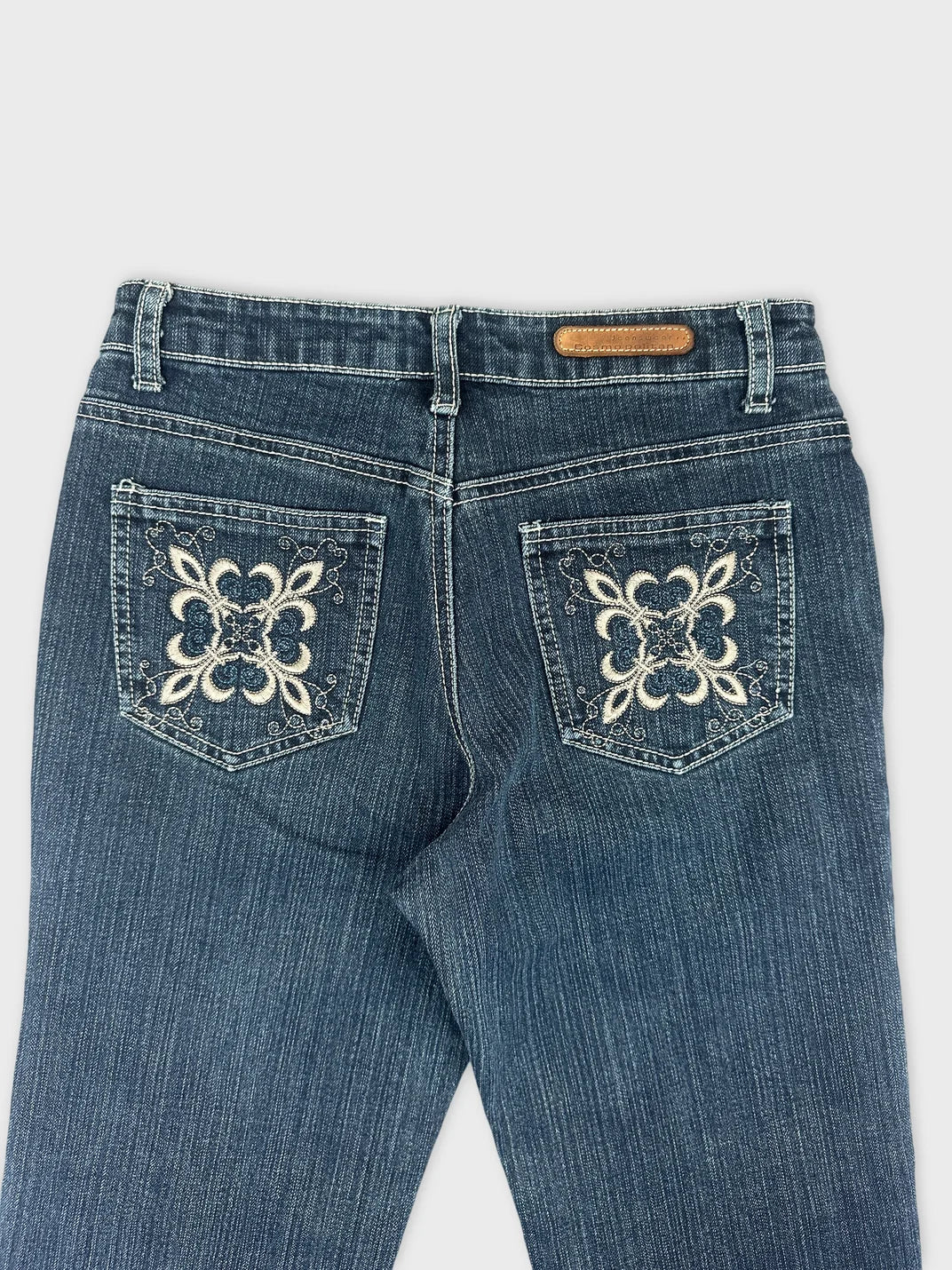Detail view of blue denim jeans featuring embroidered back pockets.