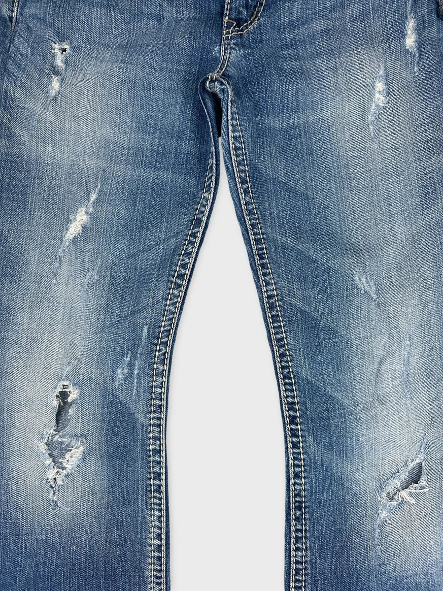 Detail view of women denim jeans in light blue with distressed patches.